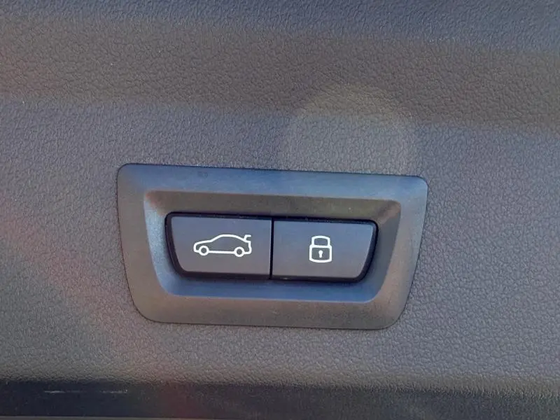 Boutons de commande pour ouverture du coffre et verrouillage, sur panneau intérieur noir texturé d’une BMW Série 1 M Brooklyn Grey.