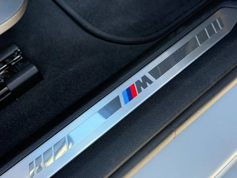 Gros plan sur la plaque de seuil de porte M Sport en métal avec logo tricolore, intérieur noir d'une BMW Série 1 M Brooklyn Grey.