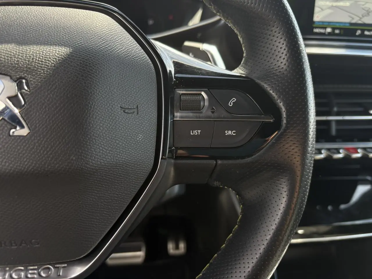Gros plan sur le volant cuir perforé noir du Peugeot 2008 GT 2021, avec commandes multimédia et surpiqûres vertes visibles.