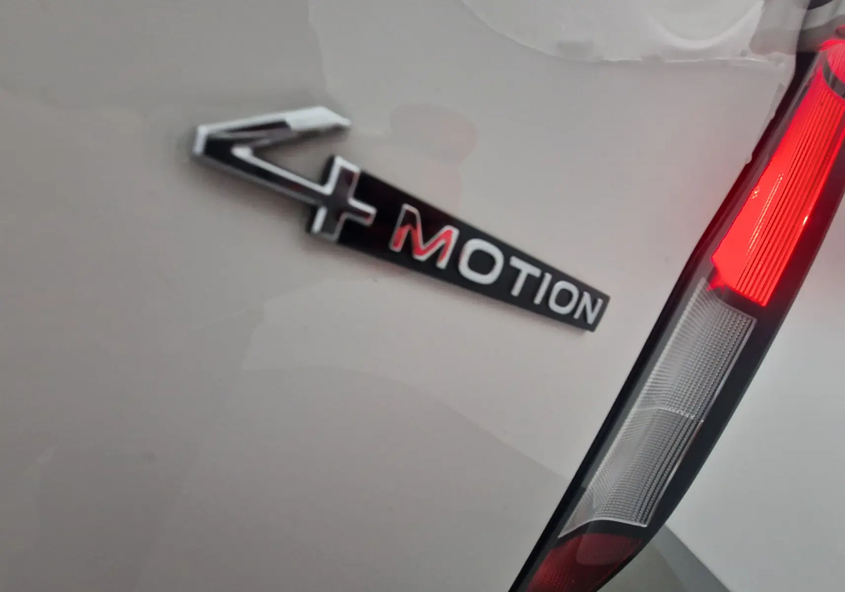 Gros plan sur l'emblème 4MOTION et le feu arrière droit d'un Volkswagen Caddy Maxi blanc.