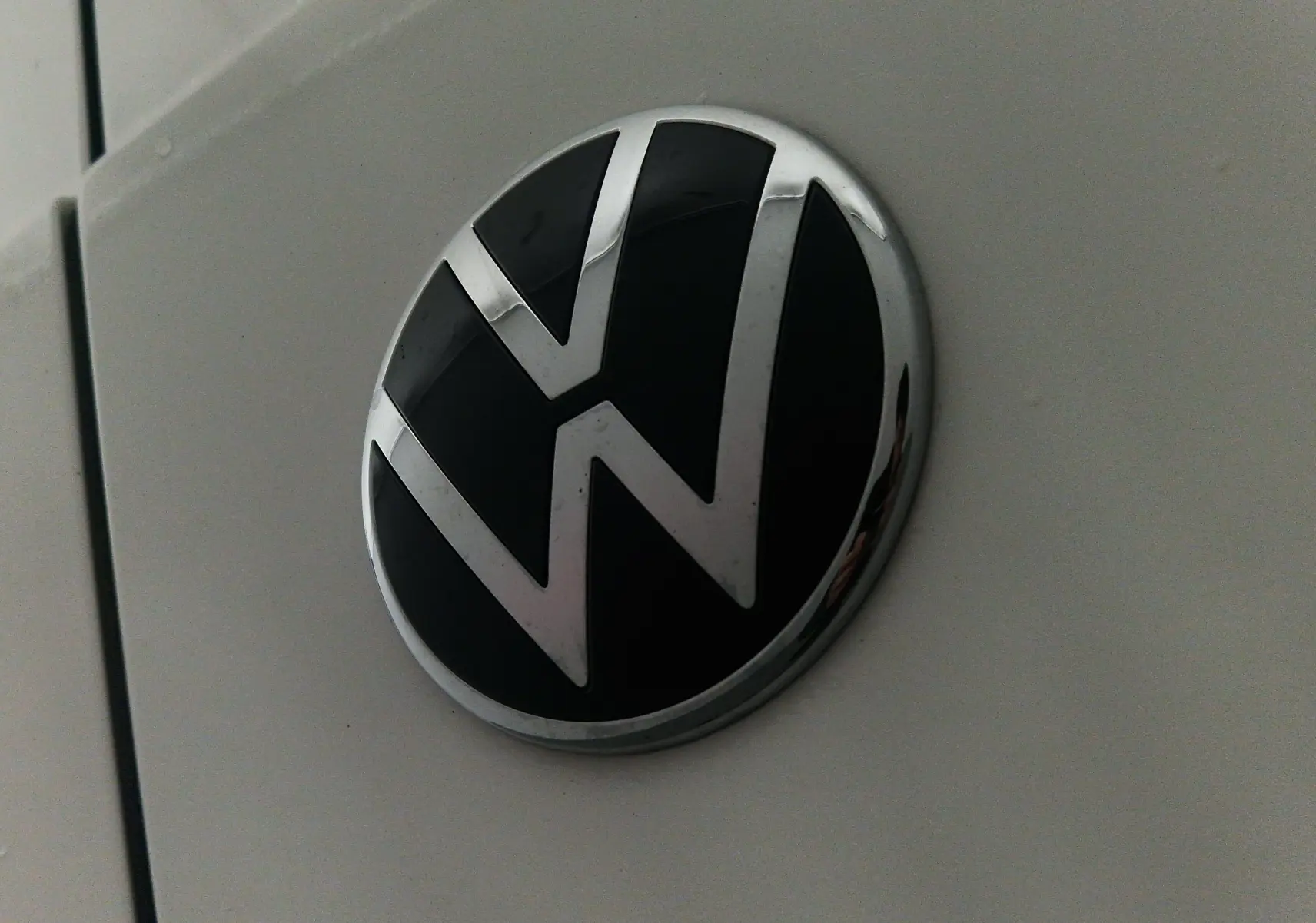 Gros plan sur le logo Volkswagen noir et chrome sur la carrosserie blanche du Caddy Maxi 4 Motion 2025.