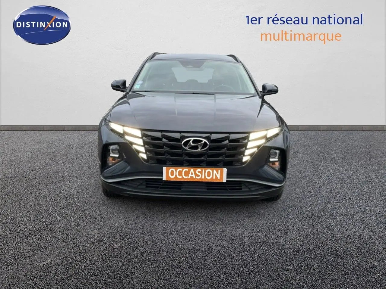 Vue frontale d'un Hyundai Tucson 2023 hybride en Dark Knight Metal avec feux LED allumés sur fond neutre.