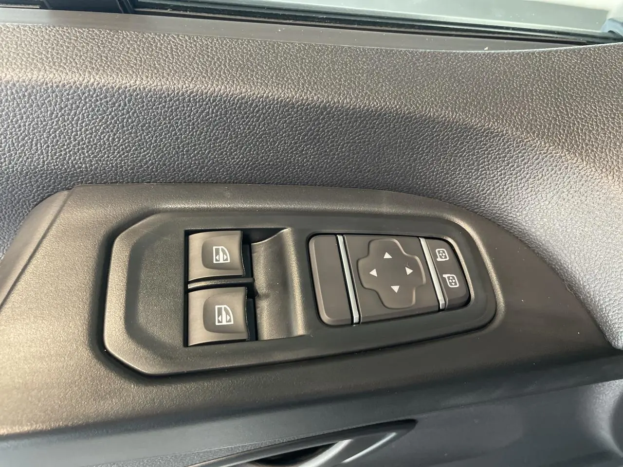 Gros plan sur les commandes de lève-vitres et réglage des rétroviseurs côté conducteur du Renault Trafic Fourgon gris Comète.