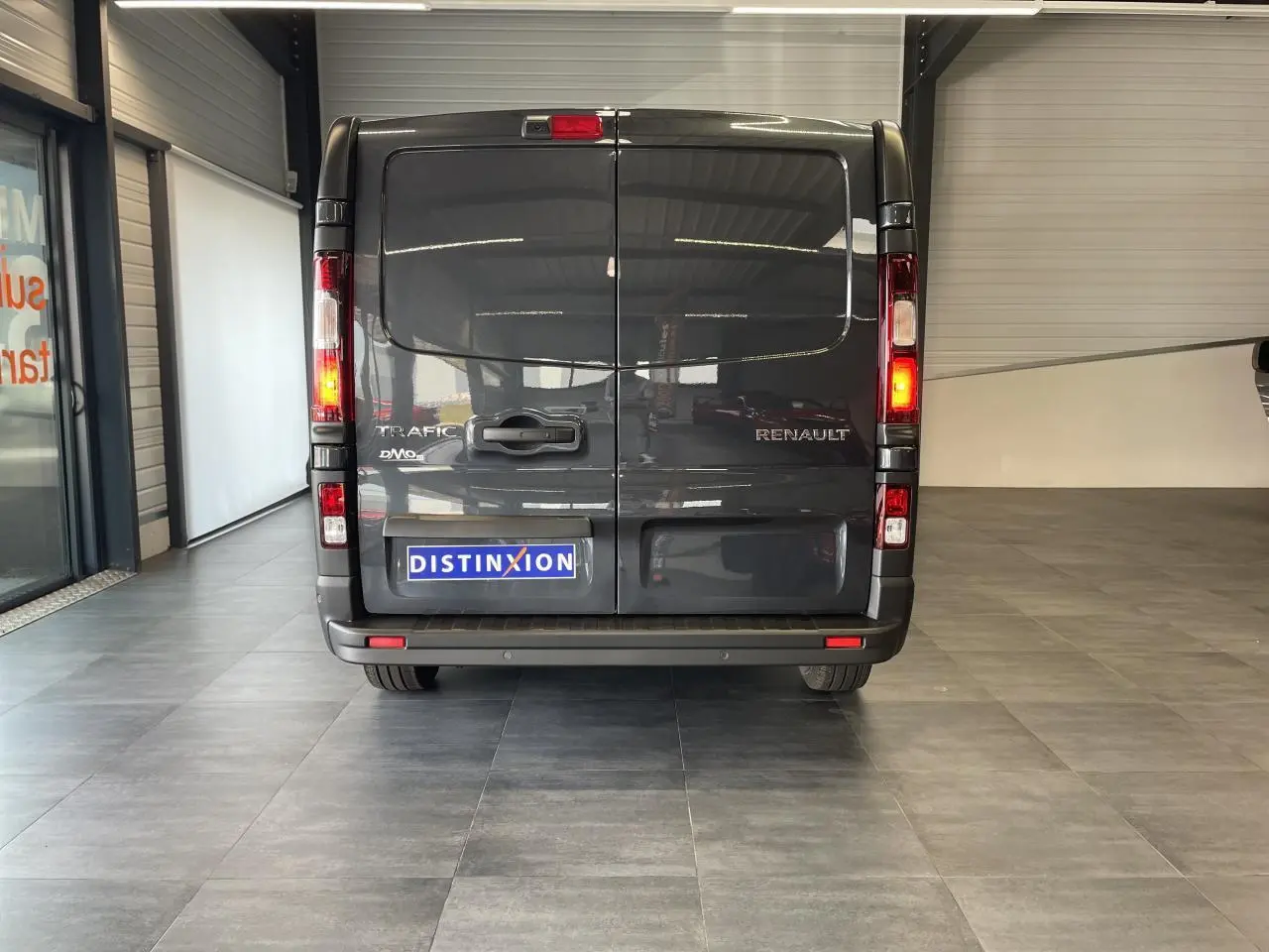 Vue arrière d’un Renault Trafic Fourgon gris comète avec feux allumés dans un showroom intérieur.