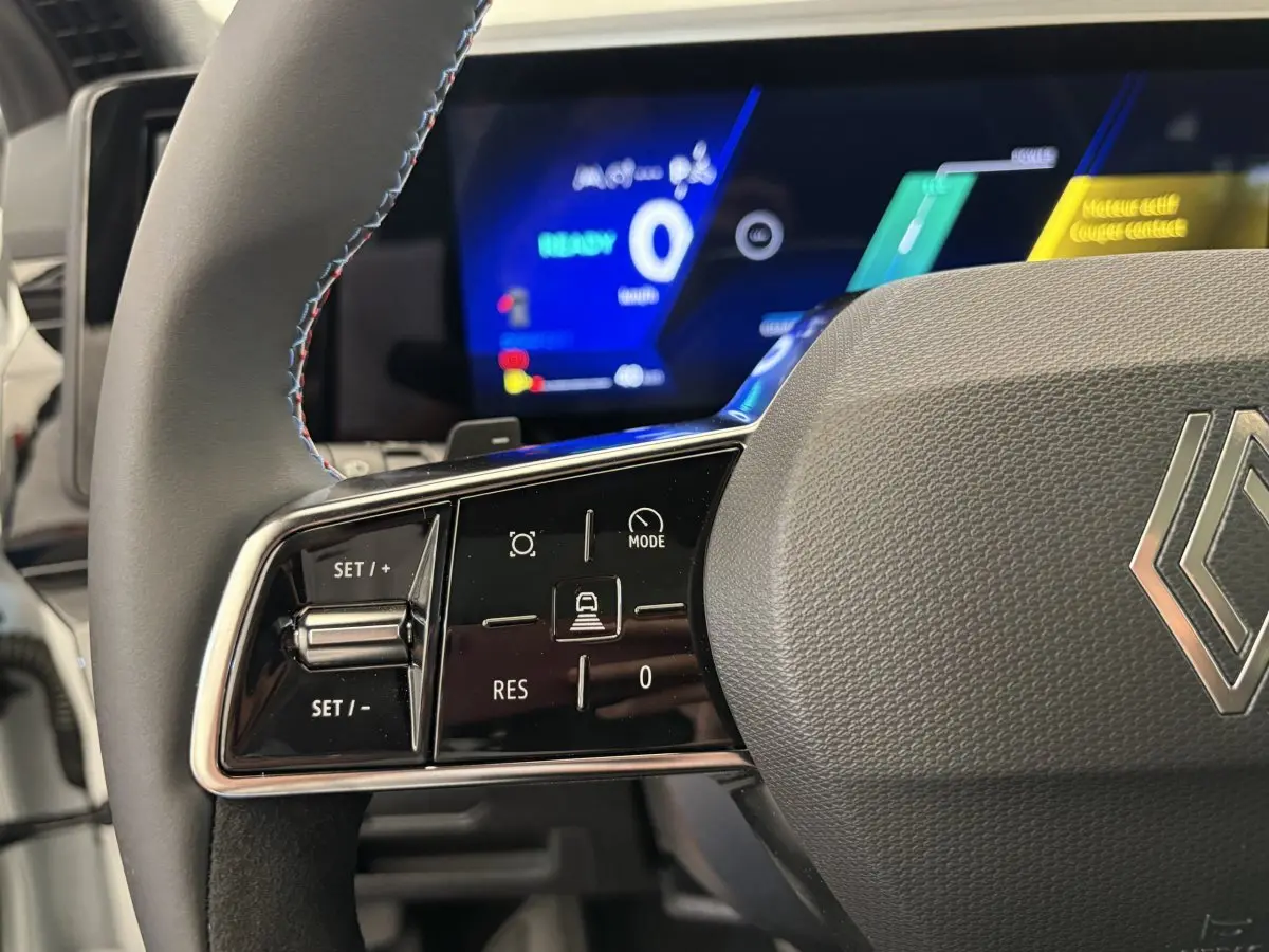 Gros plan sur le volant en cuir suédé avec commandes multifonctions du Renault Espace blanc, affichage numérique en arrière-plan.