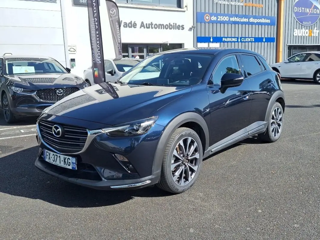 Mazda CX-3 bleu en 3/4 avant droit, avec jantes aluminium et calandre chromée visible en extérieur.