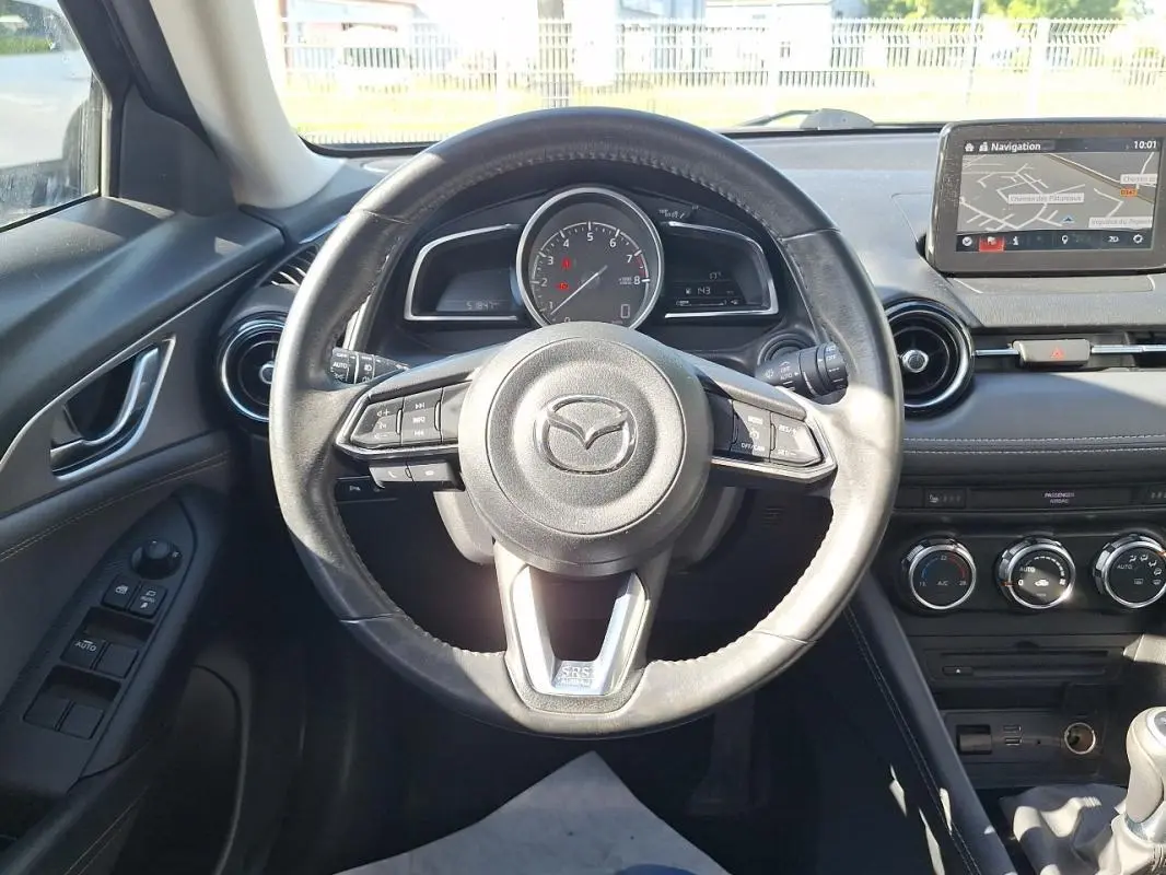 Vue intérieure centrée sur le volant cuir multifonctions d'une Mazda CX-3 2021 avec écran tactile GPS visible.