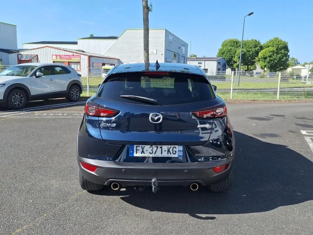 Vue arrière d'un Mazda CX-3 bleu avec attelage et double sortie d'échappement, stationné en extérieur.