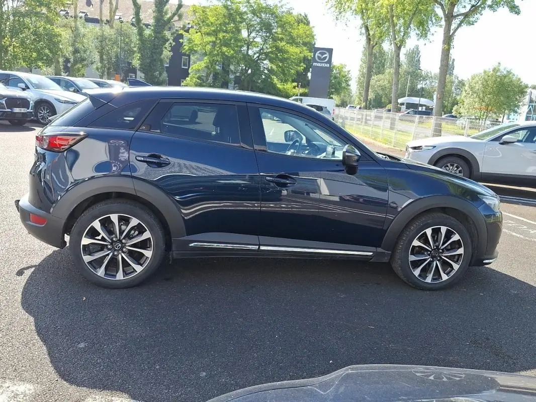Vue de profil côté gauche d'un Mazda CX-3 bleu 2021 avec jantes alliage et vitres surteintées.