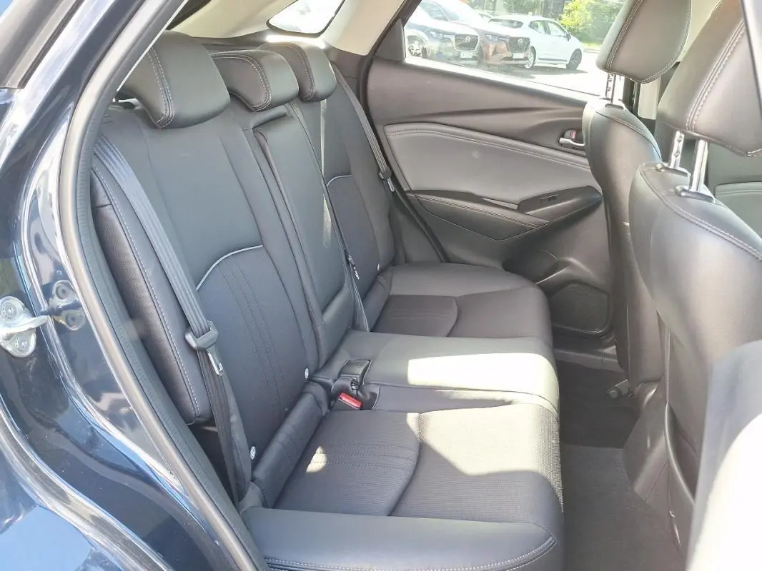 Vue intérieure côté gauche des sièges arrière noirs d'un Mazda CX-3 bleu, avec ceintures de sécurité visibles.
