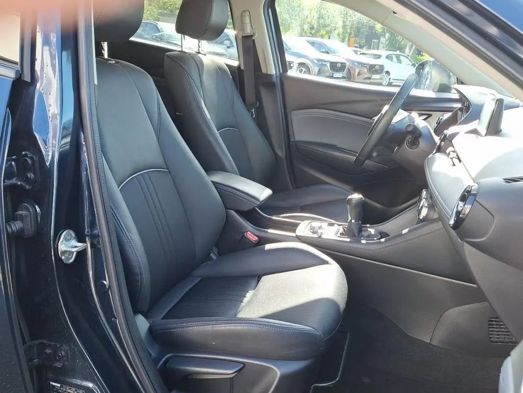 Vue intérieure côté conducteur du Mazda CX-3 bleu 2021, sièges en cuir noir et console centrale avec boîte manuelle.