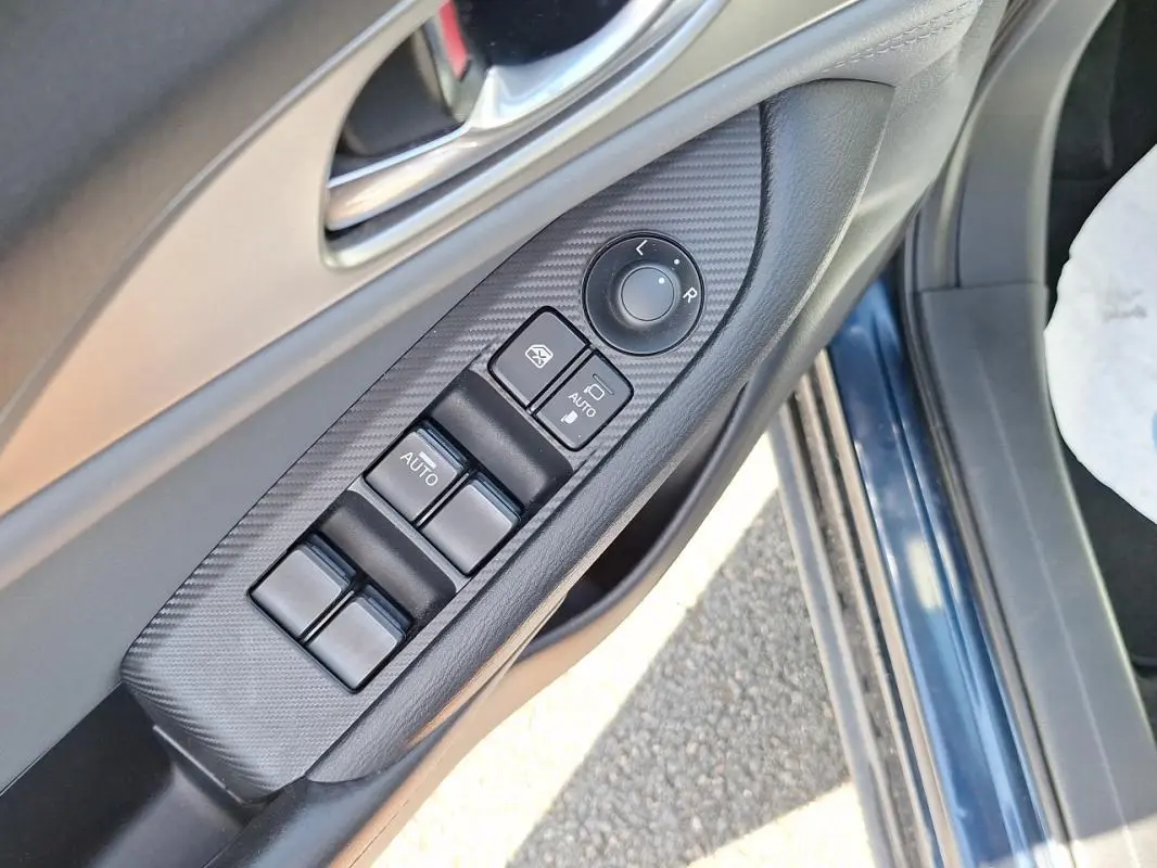 Gros plan sur la commande des vitres et rétroviseurs côté conducteur d’une Mazda CX-3 bleu 2021.