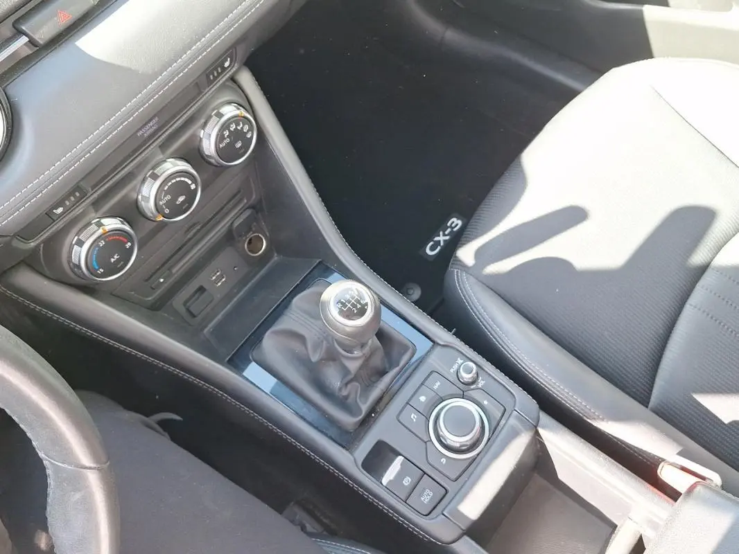 Vue intérieure en plongée du levier de vitesse manuel et console centrale noire du Mazda CX-3 2021.