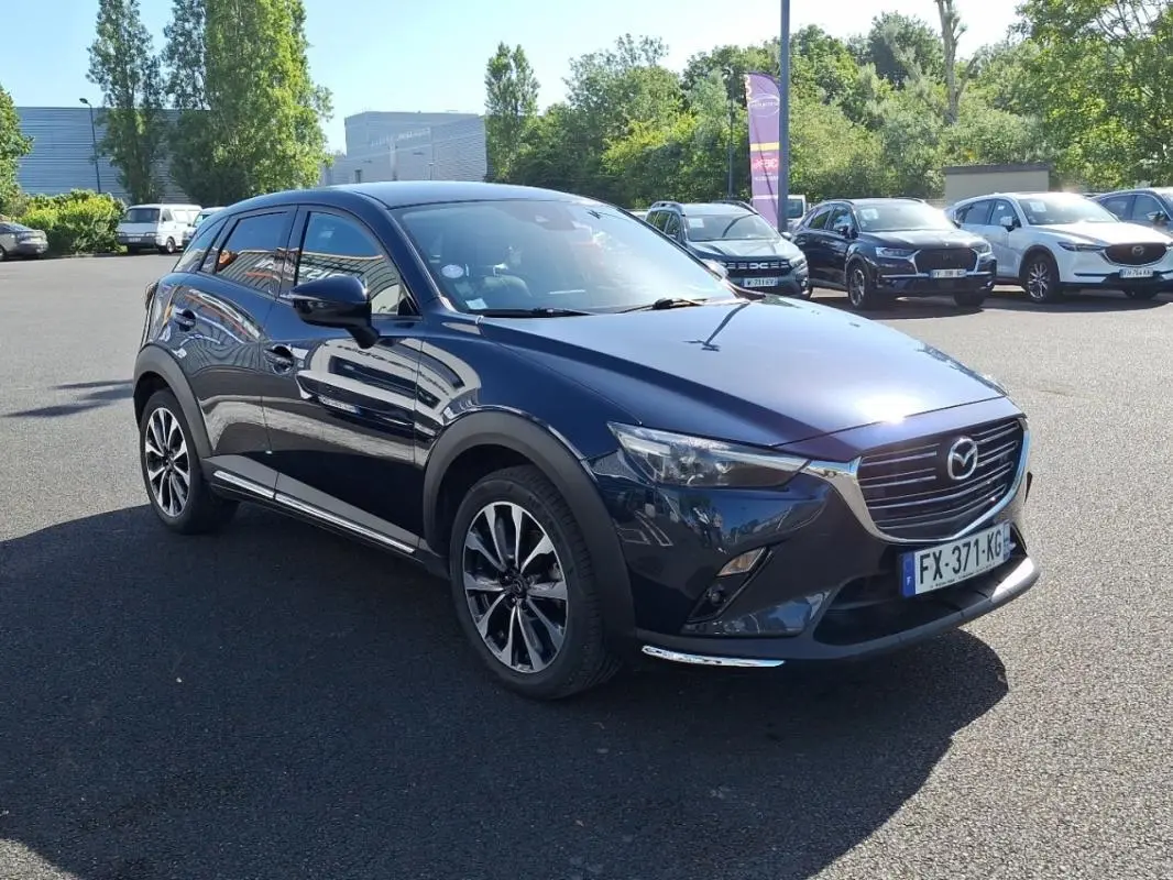 Mazda CX-3 bleu foncé vue 3/4 avant droit, jantes alliage et calandre chromée visible en extérieur.