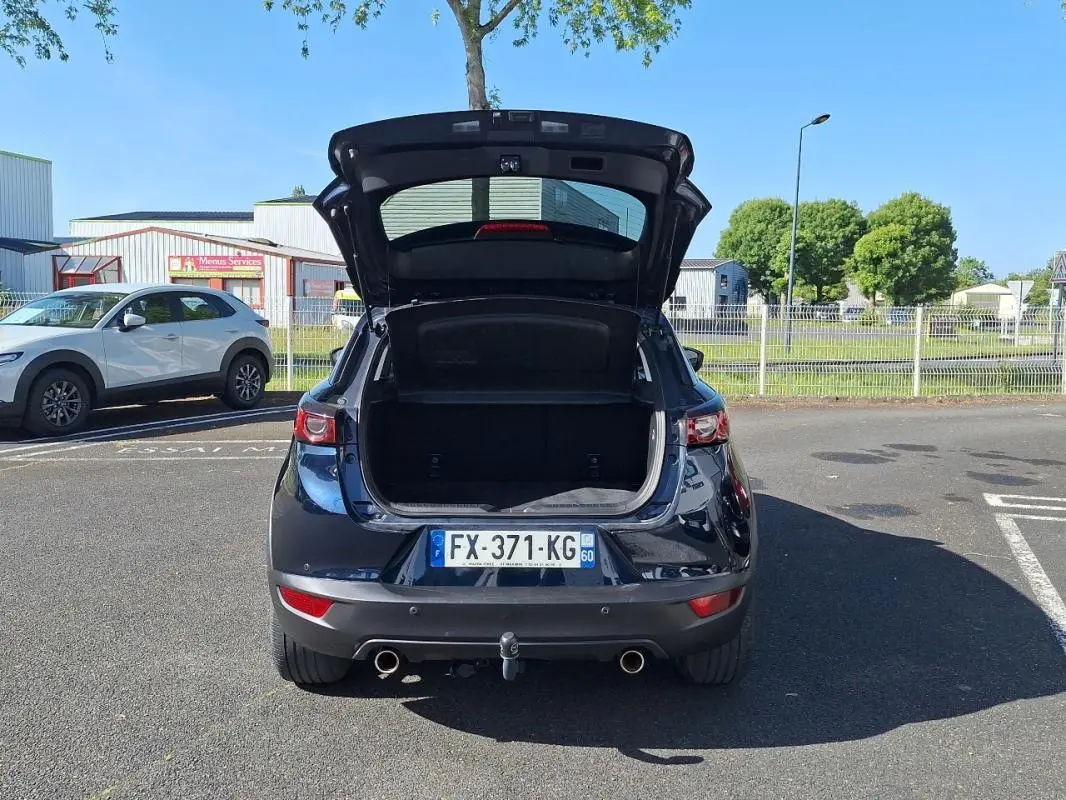 Vue arrière d'un Mazda CX-3 bleu 2021 avec coffre ouvert et attelage visible en stationnement.