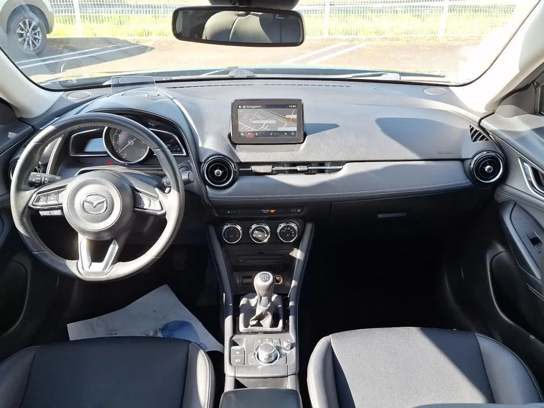 Vue intérieure frontale du tableau de bord noir du Mazda CX-3 2021 avec volant cuir multifonctions et écran tactile GPS.