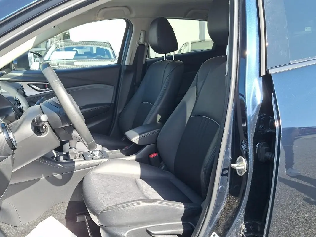 Vue intérieure côté conducteur du Mazda CX-3 bleu 2021, sièges en cuir noir et volant multifonctions visible.