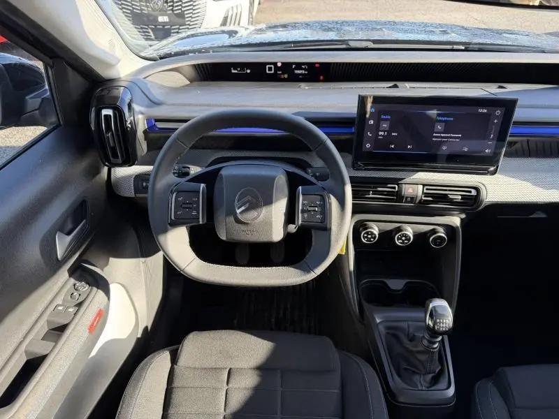 Vue intérieure du poste de conduite de la Citroën C3 1.2 Turbo 100ch PLUS 2025, volant compact et écran tactile central.