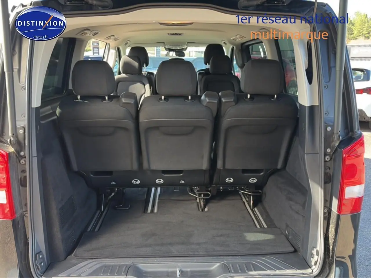 Vue arrière du coffre ouvert d’un Mercedes Classe V 220 d long noir, montrant les sièges arrière en tissu noir.