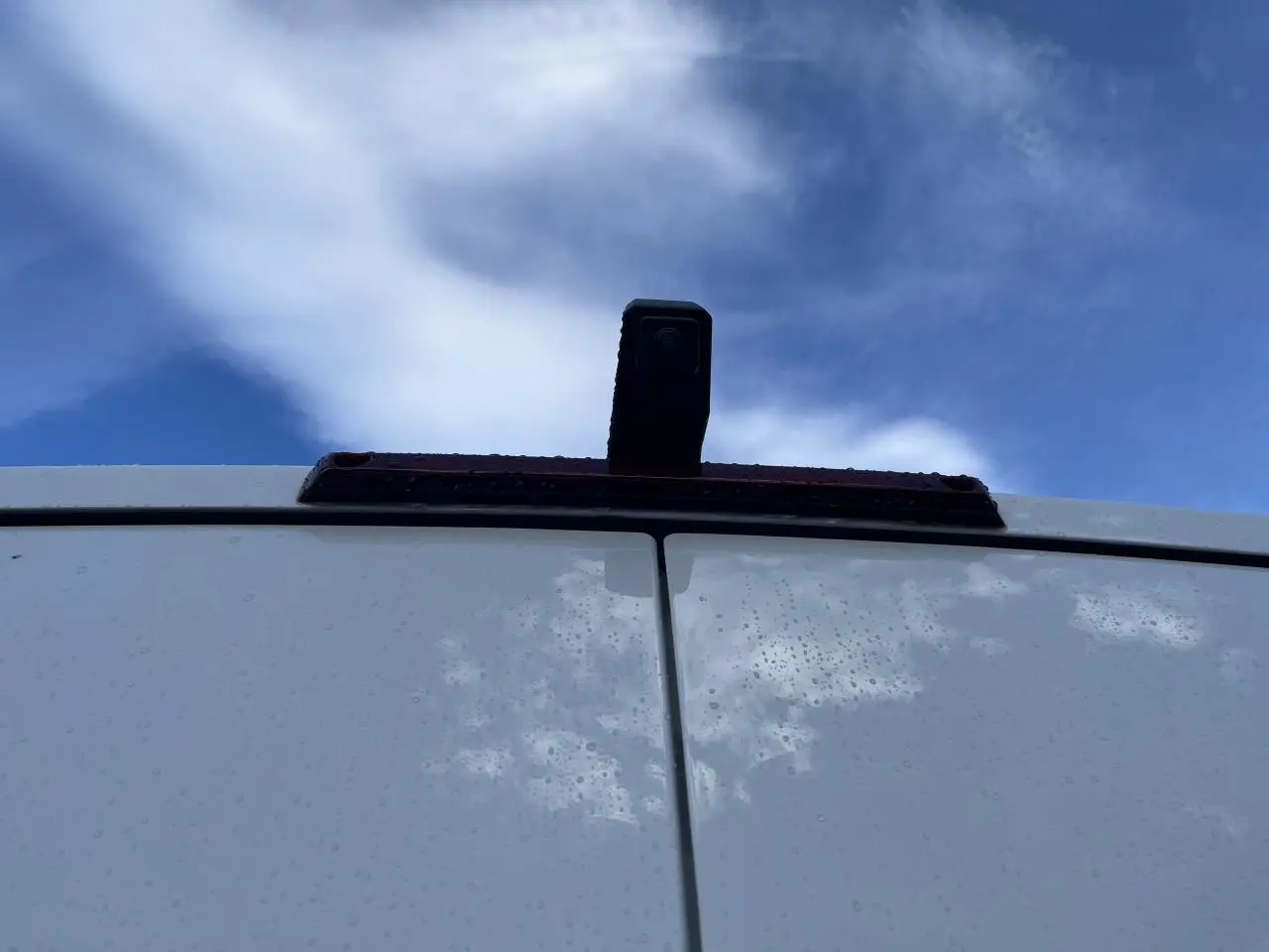 Vue rapprochée des portes arrière blanches du Renault Master 2025 avec caméra de recul sous ciel nuageux.