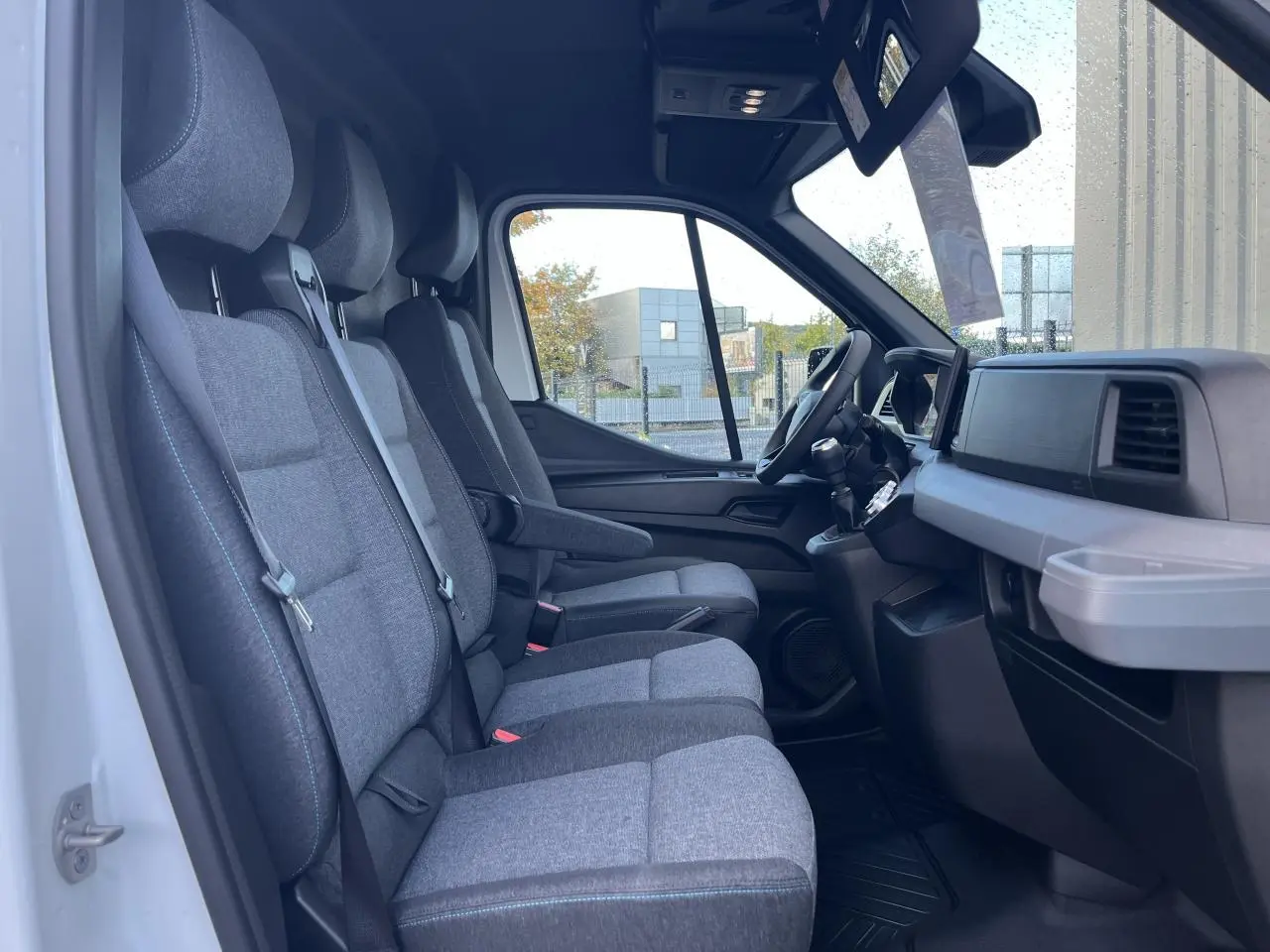 Vue intérieure côté droit du Renault Master 2025, montrant la banquette 3 places en tissu gris avec surpiqûres bleues.