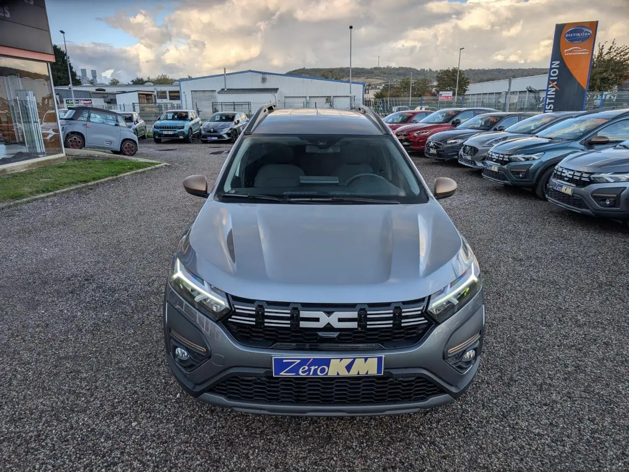 Vue avant d'un Dacia Jogger gris métallisé avec calandre noire et feux LED allumés sur un parking extérieur.