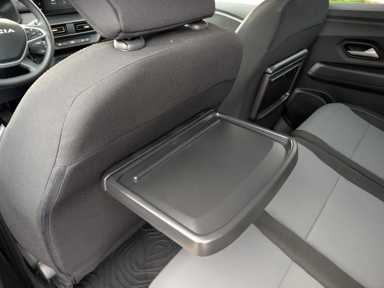 Dacia Jogger gris, vue intérieure arrière côté droit montrant tablette rabattable sur dossier siège avant.