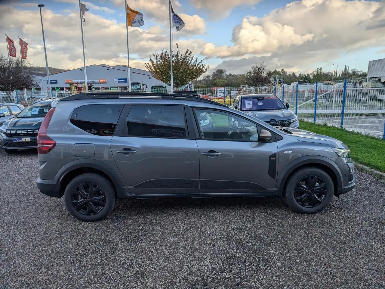 Vue de profil côté gauche d'un Dacia Jogger gris métallisé avec jantes noires et barres de toit noires.