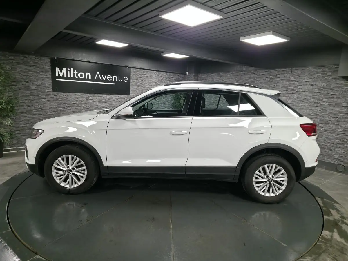 Vue de profil côté gauche d'un Volkswagen T-Roc blanc avec jantes alliage et toit ouvrant en showroom.