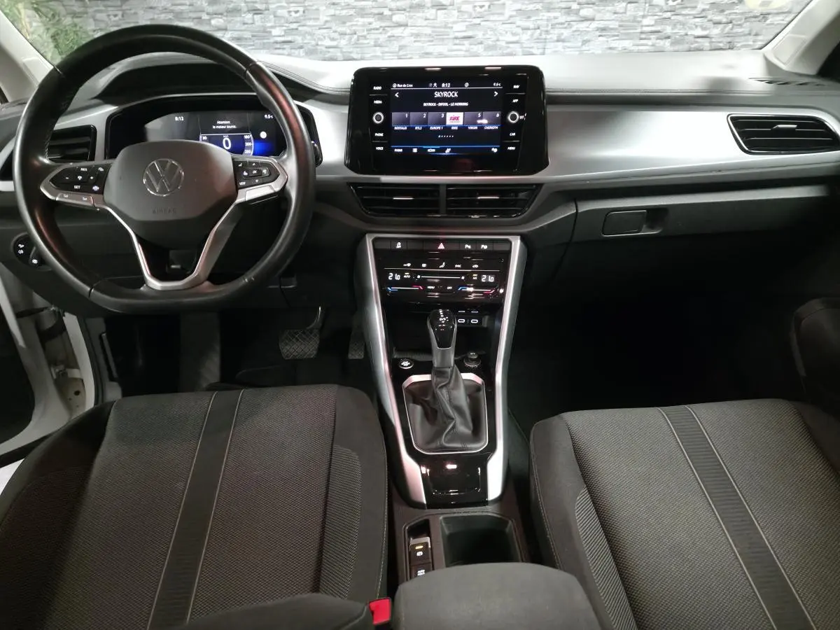 Vue intérieure avant du Volkswagen T-Roc blanc 2022, tableau de bord gris métallisé avec écran tactile et volant cuir multifonction.