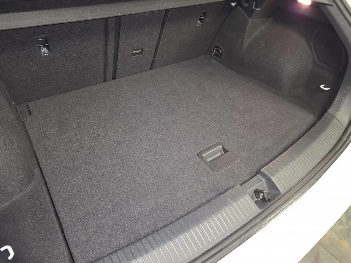 Coffre ouvert du Volkswagen T-Roc blanc, vue plongeante sur le tapis de sol noir et les fixations ISOFIX.