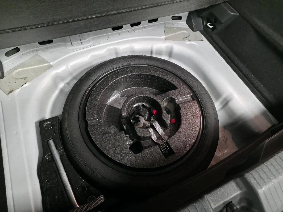 Vue plongeante sur la roue de secours et le coffre blanc du Volkswagen T-Roc 2.0 TDI 2022, avec outils de changement visibles.