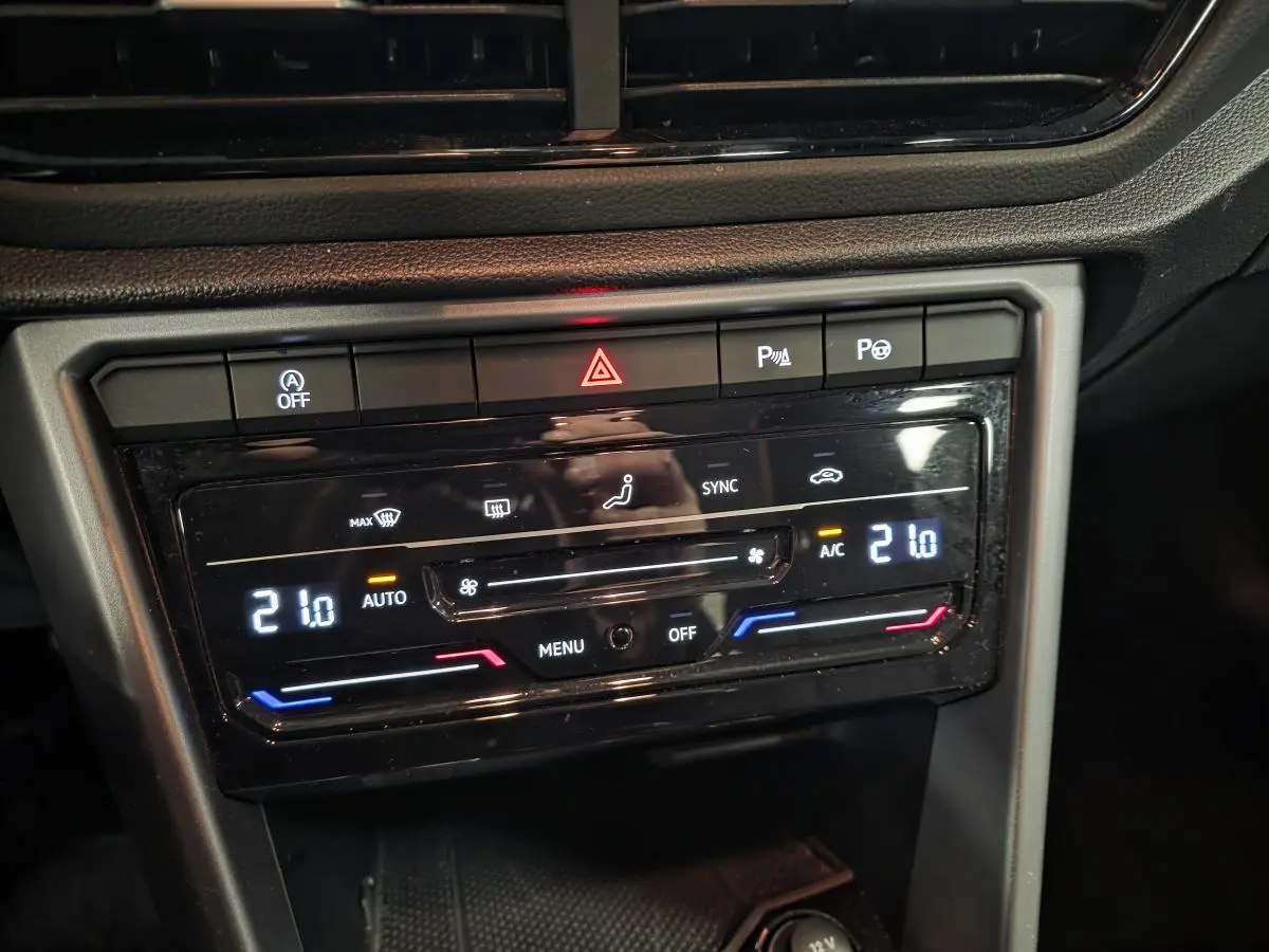 Gros plan sur la console centrale du Volkswagen T-Roc blanc, affichant la climatisation automatique bi-zone à 21°C.