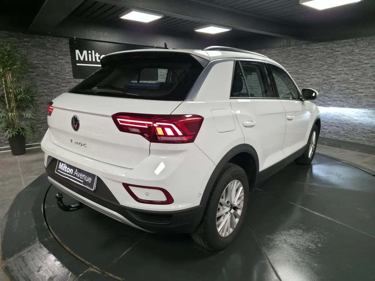 Volkswagen T-Roc blanc en 3/4 arrière droit, avec attelage amovible et feux arrière LED allumés.