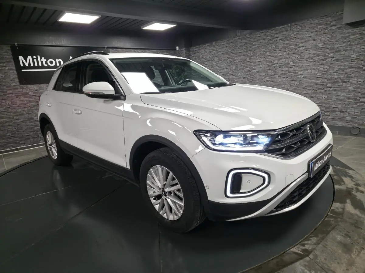 Volkswagen T-Roc blanc vue 3/4 avant droit avec phares LED allumés en intérieur showroom.