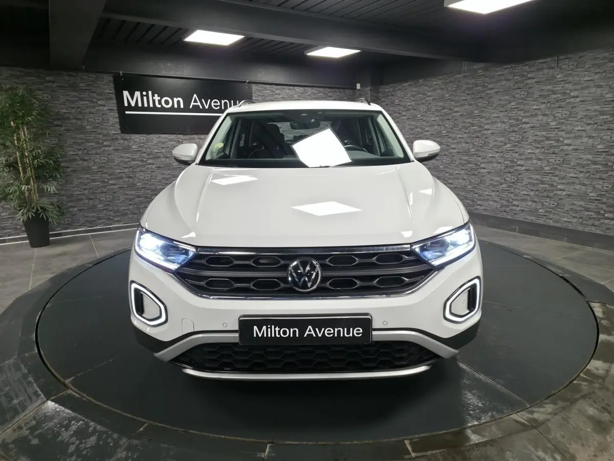 Vue avant d'un Volkswagen T-Roc blanc avec feux LED allumés dans un showroom intérieur.