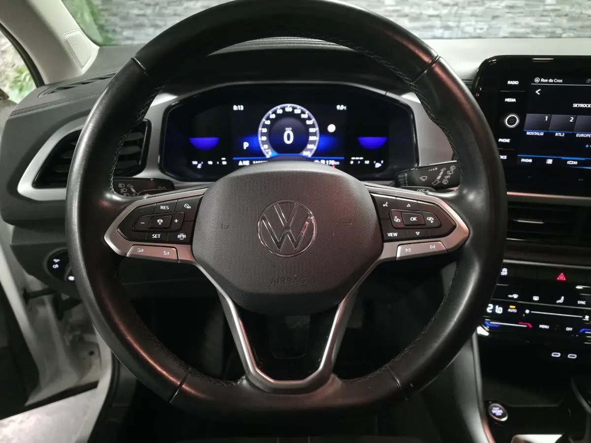 Vue rapprochée du volant en cuir noir multifonction du Volkswagen T-Roc blanc avec tableau de bord digital allumé.