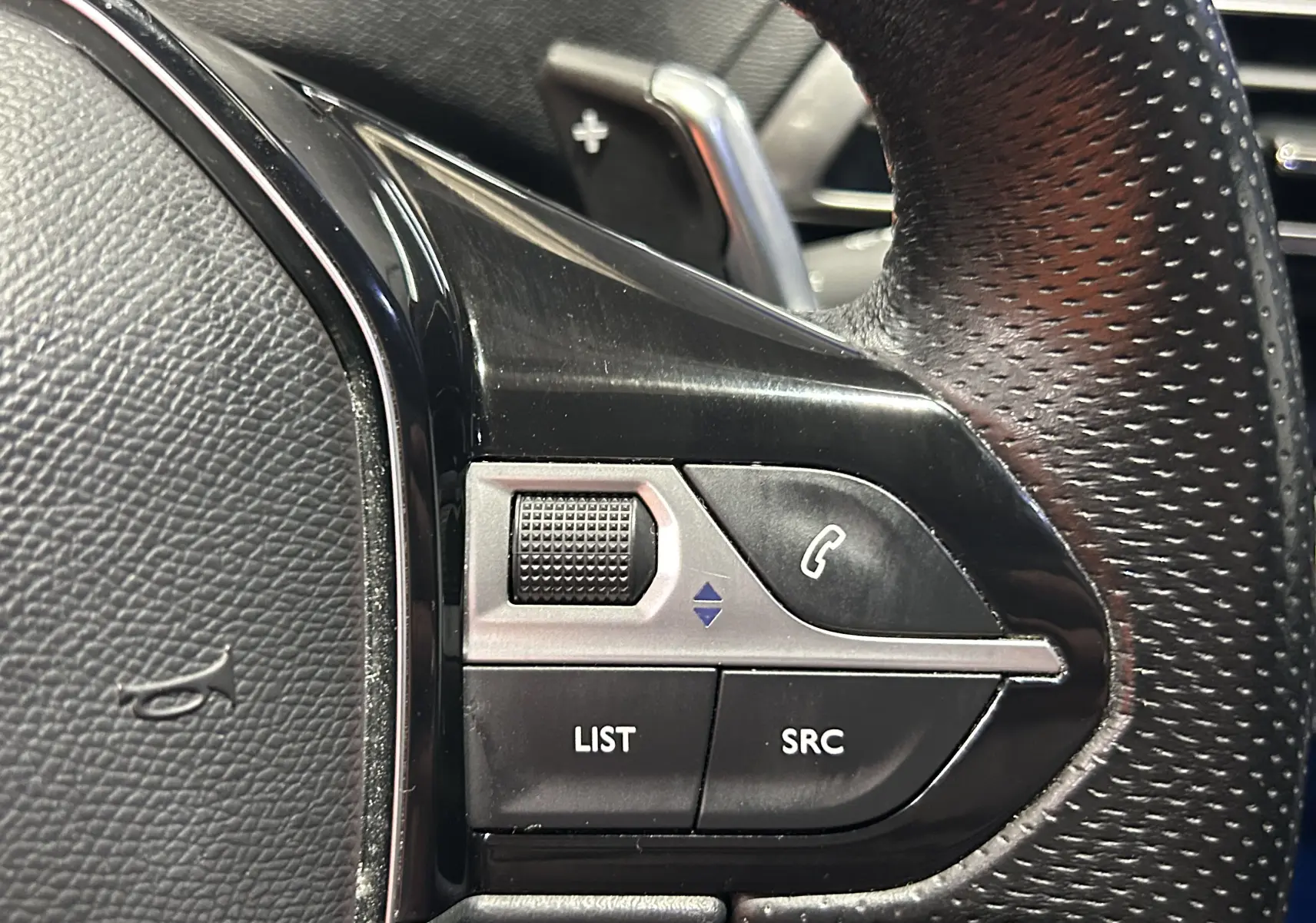 Gros plan sur les commandes gauche du volant perforé du Peugeot 3008 blanc, avec molette et boutons fonction audio.
