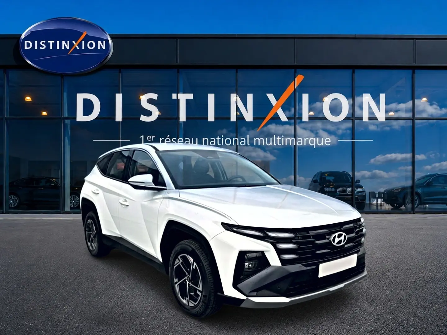 Vue 3/4 avant droit du Hyundai Tucson blanc 2026 avec calandre noire et jantes alliage 17 pouces devant un showroom Distinxion.