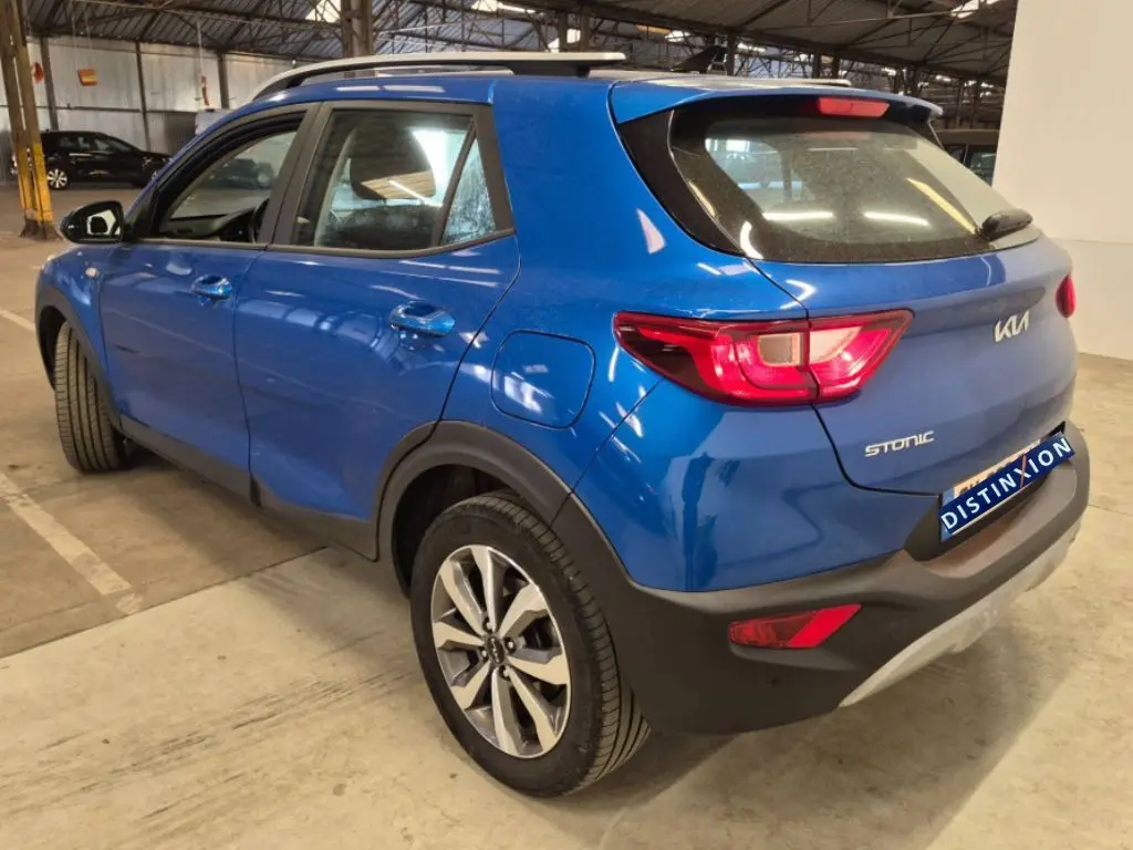 Vue 3/4 arrière droite du KIA Stonic bleu 2024 avec feux arrière allumés et jantes alliage distinctives.