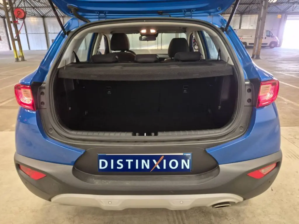 Vue arrière d’un KIA STONIC bleu 2024 avec coffre ouvert, mettant en valeur l’espace de chargement et les feux arrière allumés.