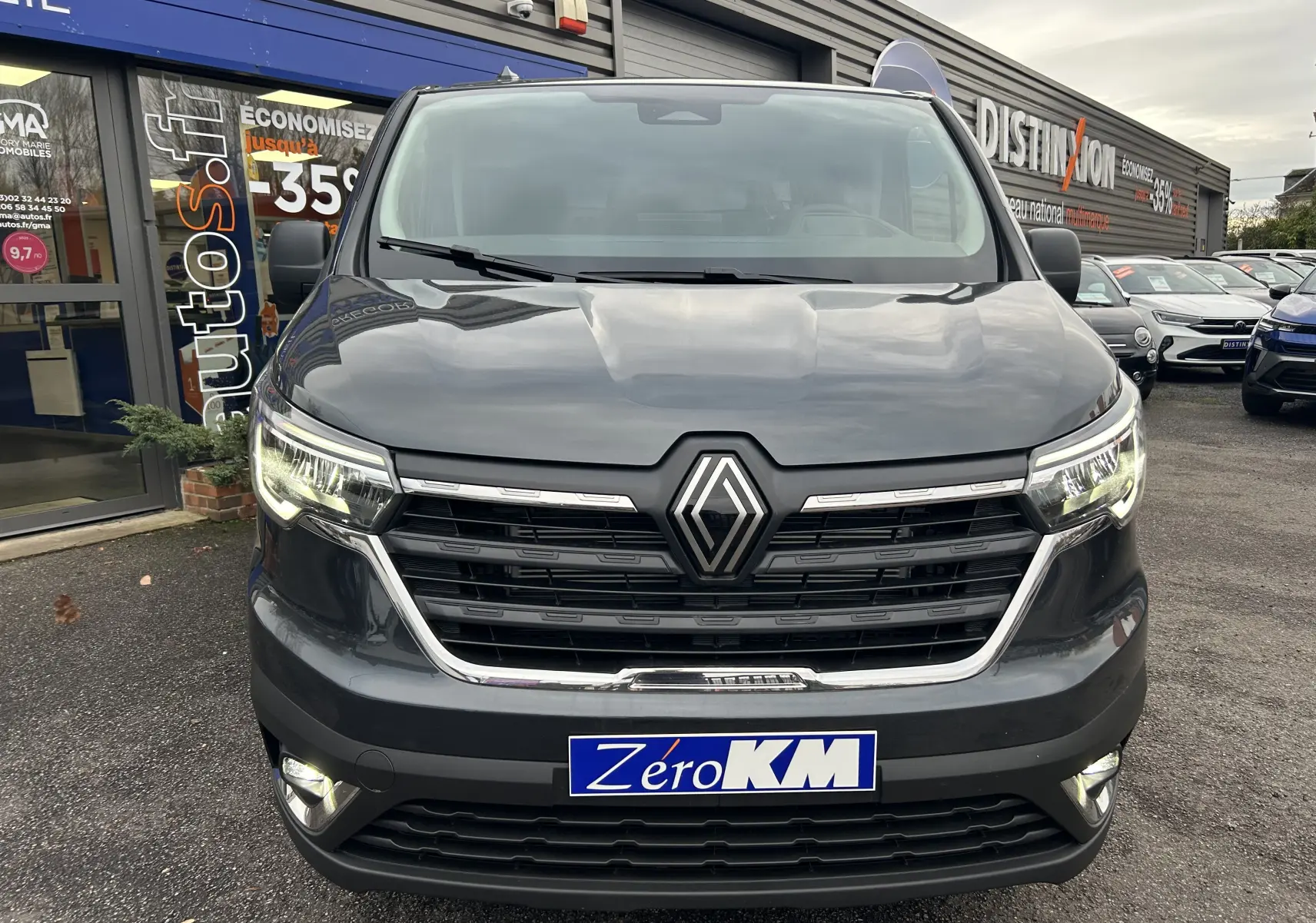 Vue frontale d’un Renault Trafic Fourgon Advance gris Comète avec phares allumés et plaque Zéro KM.