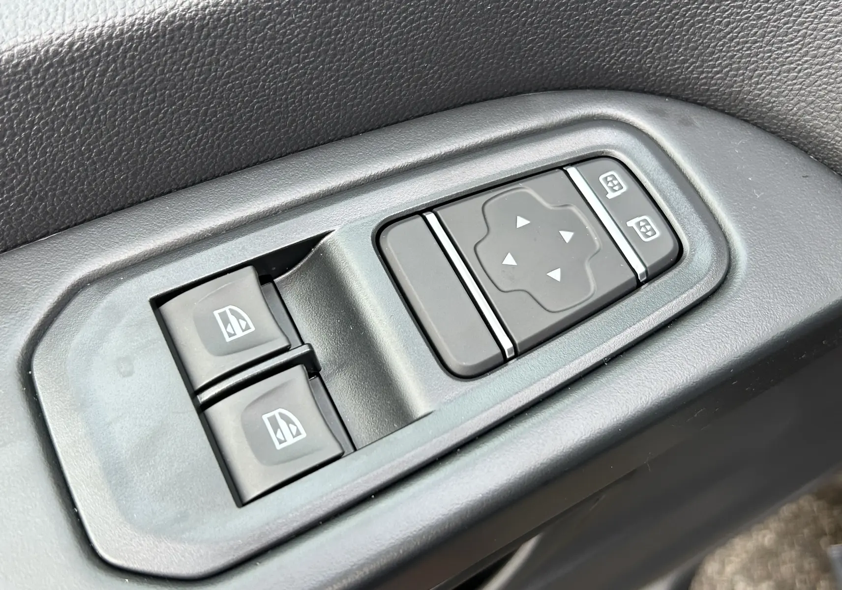 Gros plan sur les commandes de réglage des vitres et des rétroviseurs du Renault Trafic Fourgon gris Comète, côté conducteur.