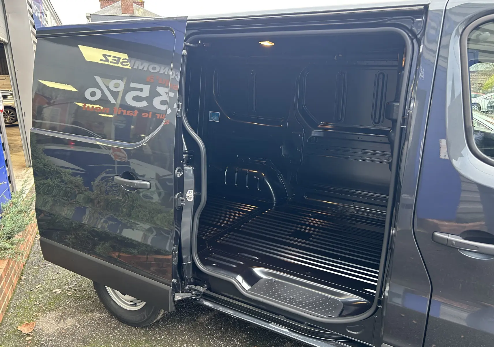 Vue latérale droite du Renault Trafic Fourgon gris Comète avec porte coulissante ouverte montrant l'intérieur vide du coffre.