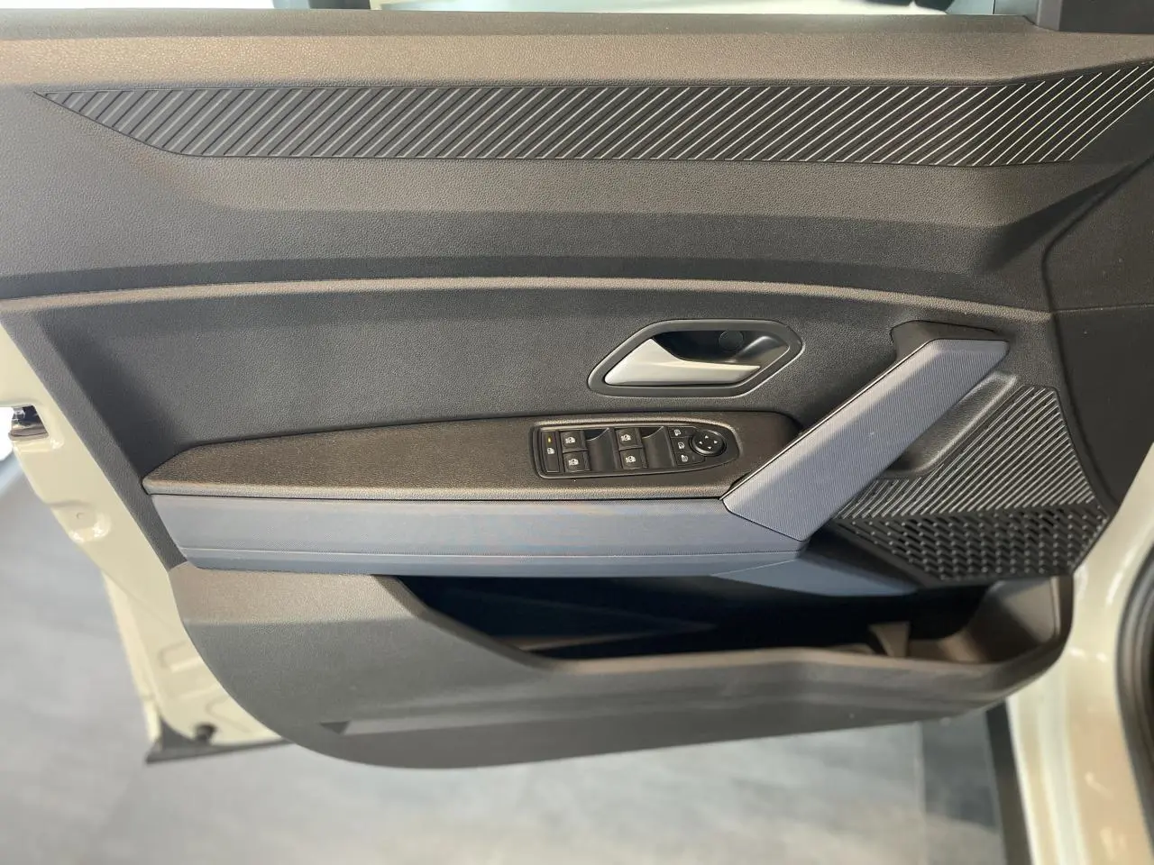 Vue latérale du panneau de porte avant gauche beige du Dacia Duster 2025 avec commandes de vitres et accoudoir Denim Bleu.