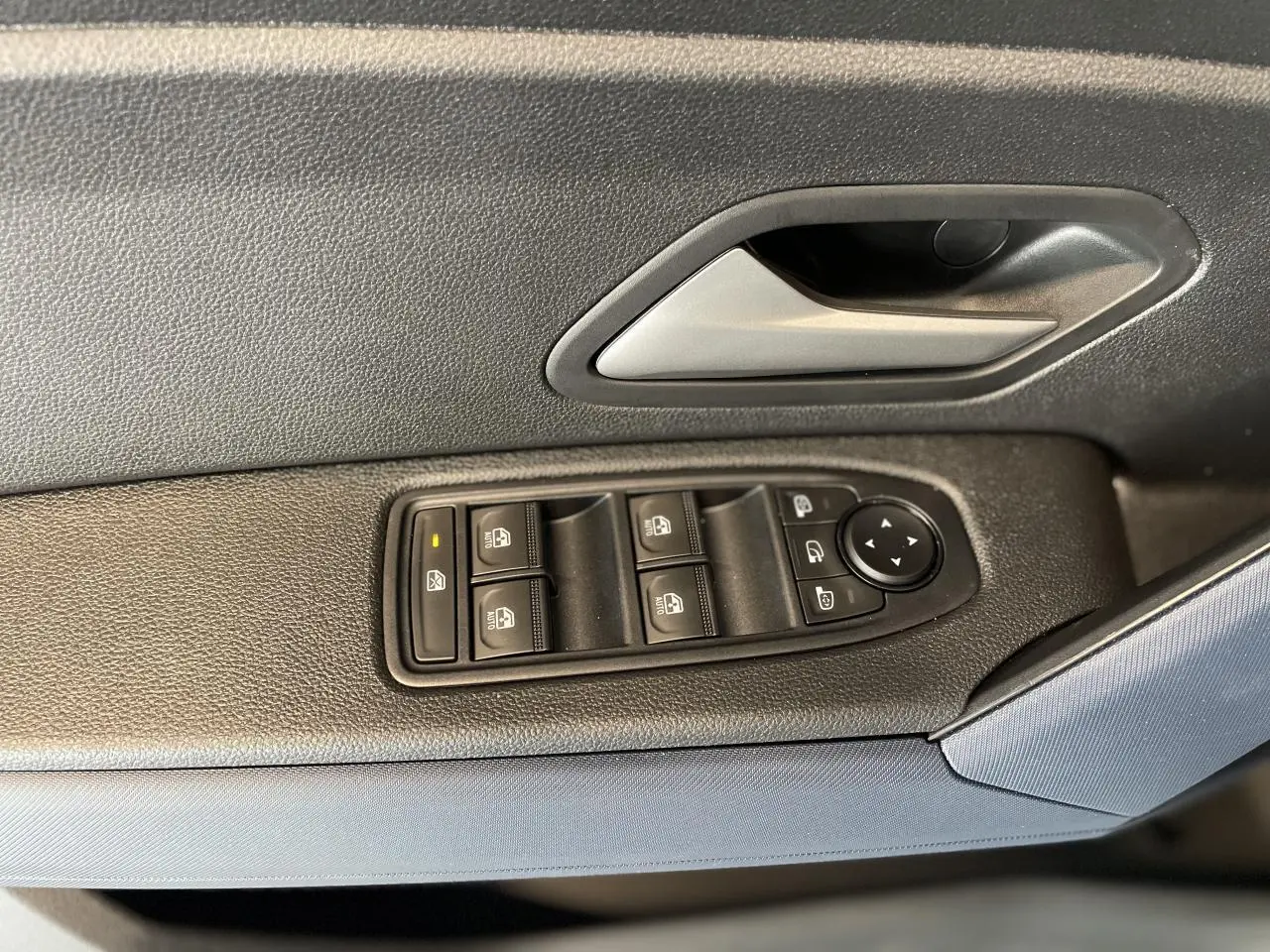 Gros plan sur la commande des vitres électriques côté conducteur d'un Dacia Duster beige avec poignée intérieure grise.