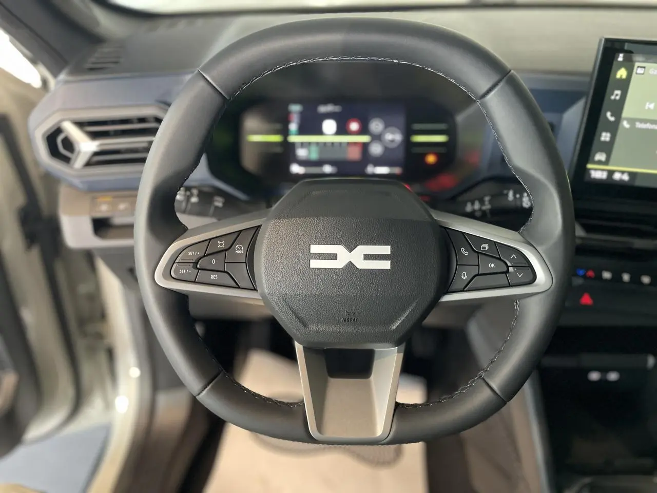 Vue rapprochée du volant noir du Dacia Duster 2025 avec commandes intégrées et tableau de bord digital en arrière-plan.
