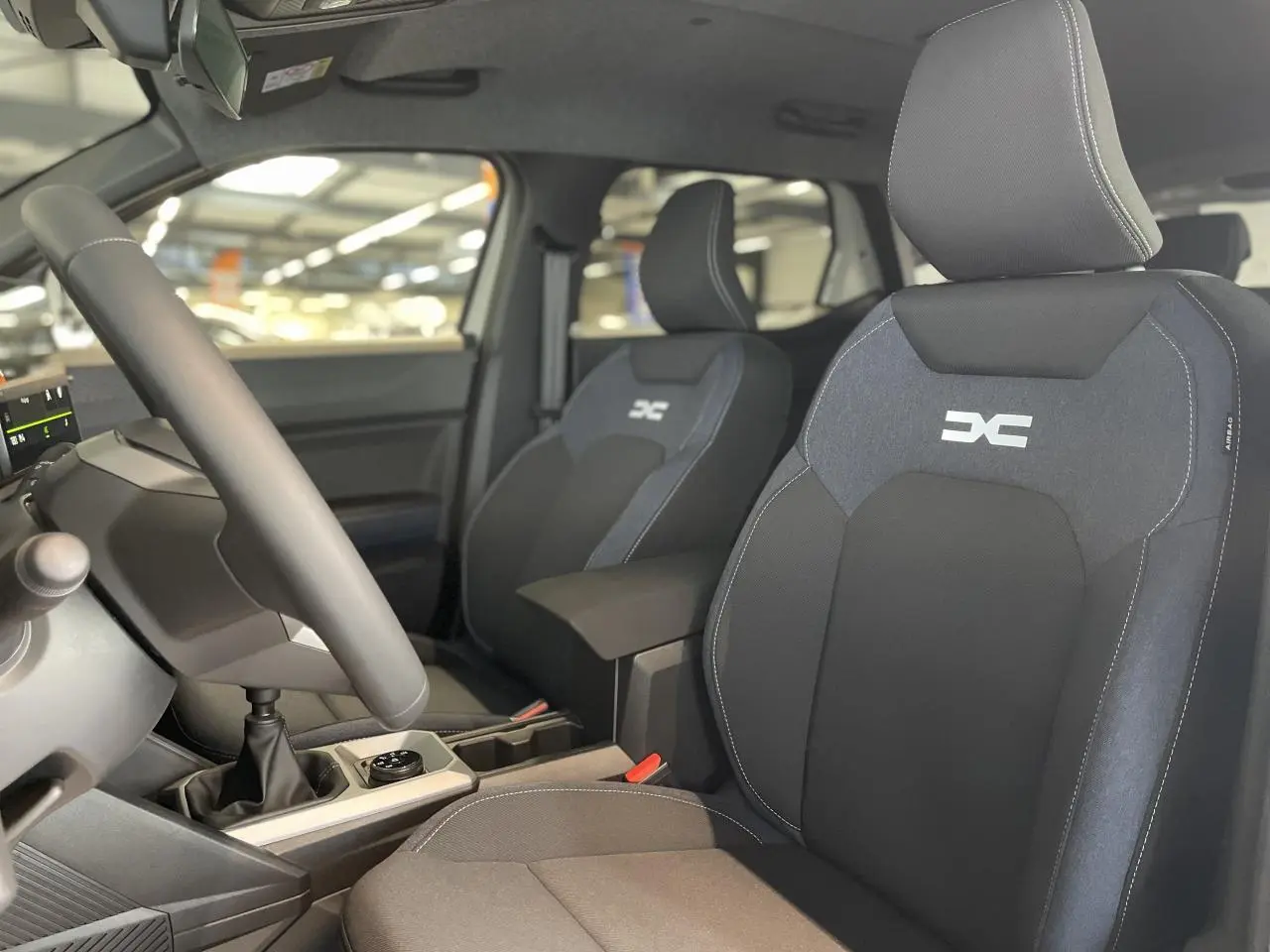 Vue intérieure avant du Dacia Duster 2025, sièges tissu Denim bleu avec logo Dacia, volant soft feel et levier de vitesses manuel.