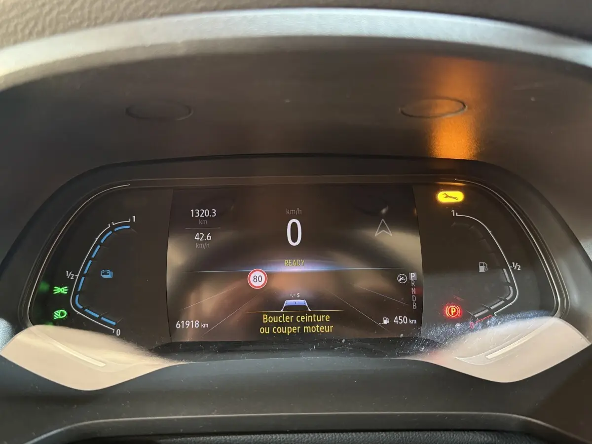 Tableau de bord numérique du Renault Captur bleu 2024, affichage multifonctions avec alertes et jauges hybrides.