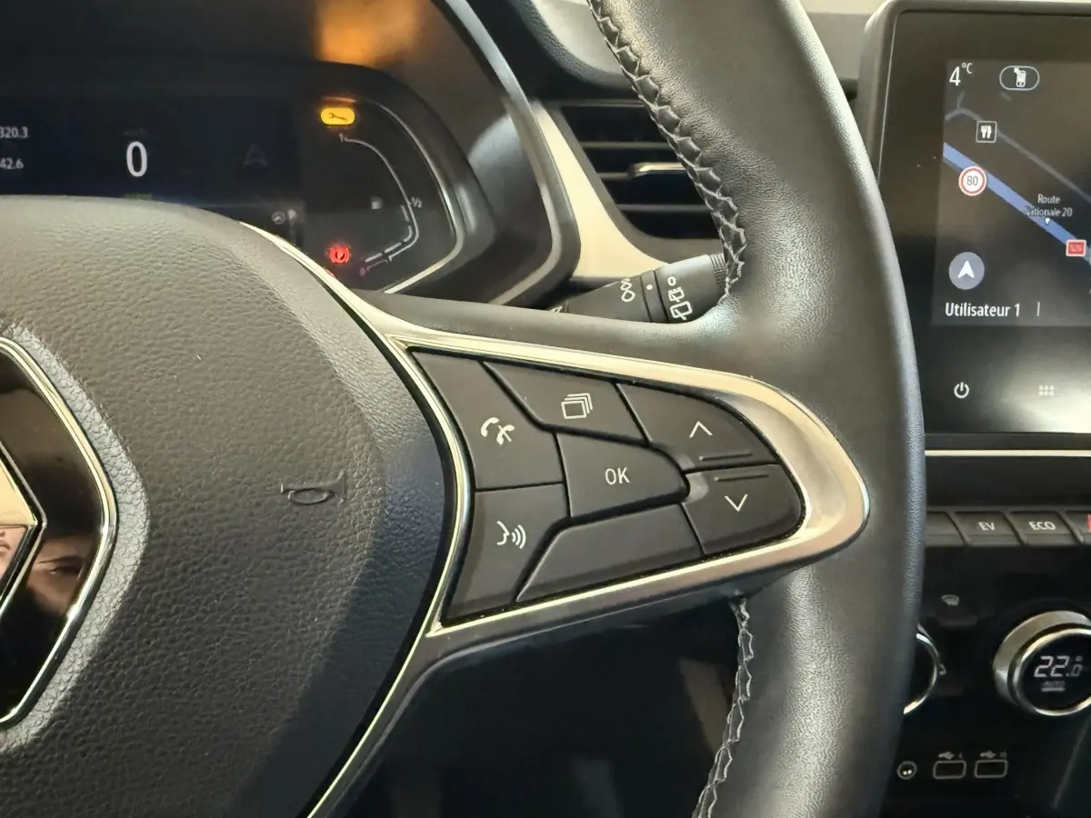 Gros plan sur le volant cuir synthétique noir du Renault Captur bleu 2024, avec commandes multifonctions et écran tactile visible.